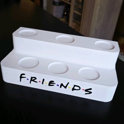 Suporte branco para velas com a palavra FRIENDS em preto com pontos coloridos