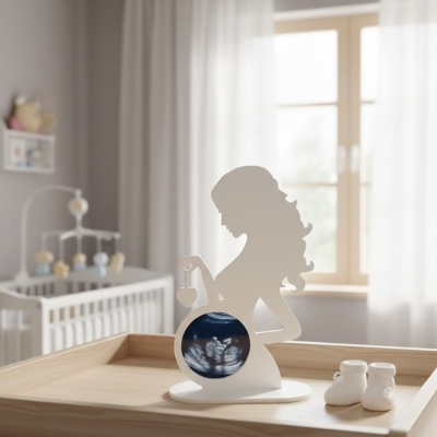 Decoração de grávida branca com inserção de ecografia, sobre superfície de madeira clara, berço ao fundo.