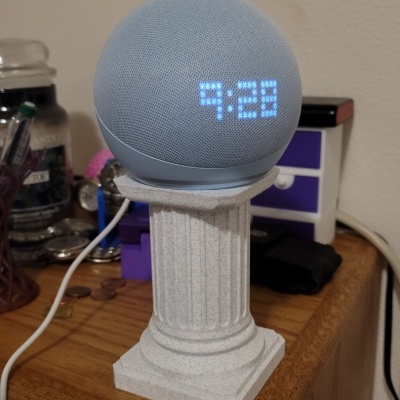 Coluna decorativa branca com relógio digital azul a mostrar 9:28 numa mesa
