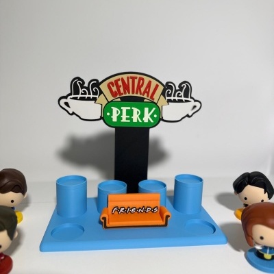 Suporte azul para figuras com sofá laranja F.R.I.E.N.D.S e placa CENTRAL PERK com quatro bonecos estilizados