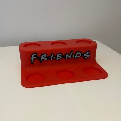 Suporte vermelho para objetos com a palavra FRIENDS escrita em letras negras com pontos coloridos.
