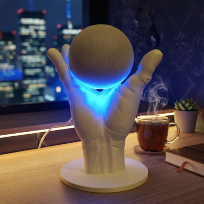 Mini coluna cinzenta em suporte mão branco com luz azul numa mesa com chá fumegante, livro e planta.