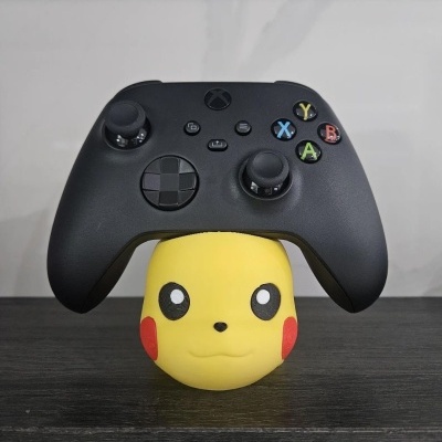 Comando de videojogo preto apoiado em figura amarela de Pikachu