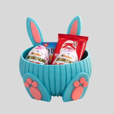 Cesto castanho em formato de coelho azul com orelhas e patas cor-de-rosa contendo ovos Kinder Überraschung e chocolates Kinder e KitKat Duo