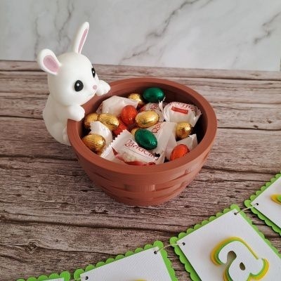 Pote castanho com coelho branco a segurar cheio de chocolates coloridos sobre mesa de madeira e fundo branco