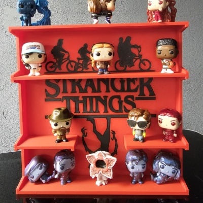 Expositor vermelho com figuras colecionáveis Funko Pop de Stranger Things e texto STRANGER THINGS no fundo.