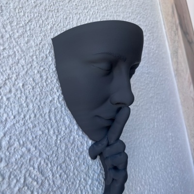 Máscara decorativa preta com mão em gesto de silêncio