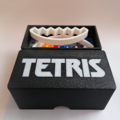 Caixa preta TETRIS com peças de plástico coloridas e brancas visíveis