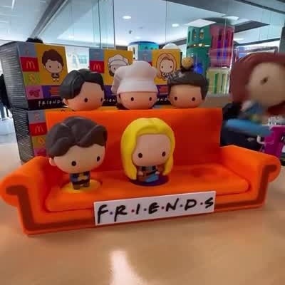 Bonecos dos personagens Friends num sofá laranja com placa FRIENDS