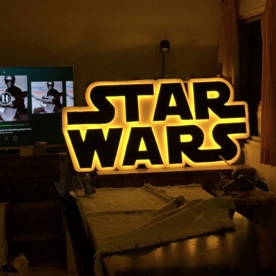 Letreiro luminoso STAR WARS em ambiente interior com mesa, cortinas e televisão.