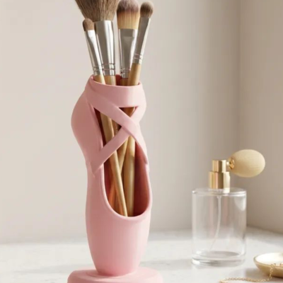 Suporte rosa de pincéis de maquilhagem em forma de sapatilha de balé com frasco de perfume e corrente dourada na mesa