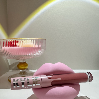 Batom líquido rosa Kylie em suporte de lábios cor-de-rosa com copo de vidro ao fundo