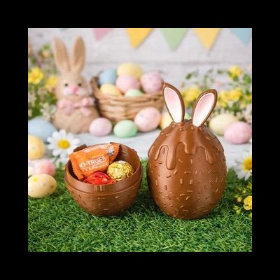 Dois ovos de chocolate, um aberto com chocolates, sobre relva artificial com decoração de coelho e ovos coloridos