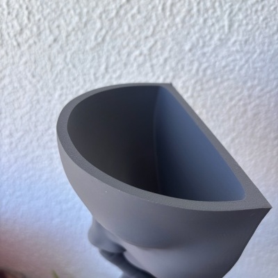 Recipiente cinza fosco com design oval e parede branca ao fundo.