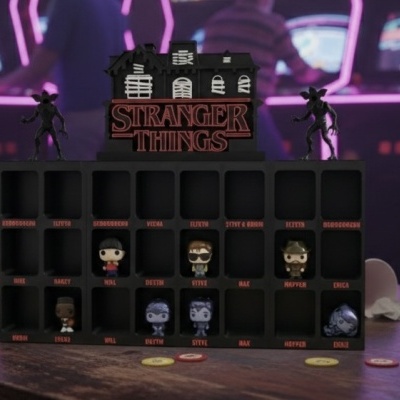 Expositor preto com figuras miniatura de Stranger Things em mesa com copos vermelhos e fundo neon.