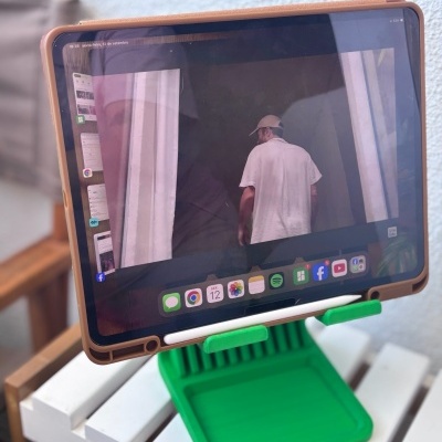Tablet com capa castanha num suporte verde sobre mesa branca, mostrando imagem de pessoa de costas