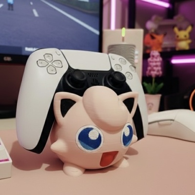 Suporte de comando com figura Pokémon Jigglypuff numa secretária com teclado, rato e auscultadores.