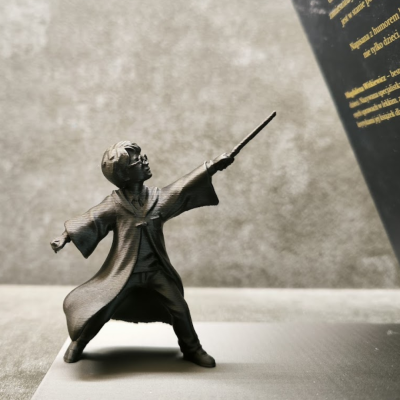 Estatueta bronzeada de menino com robe e varinha em fundo cinzento