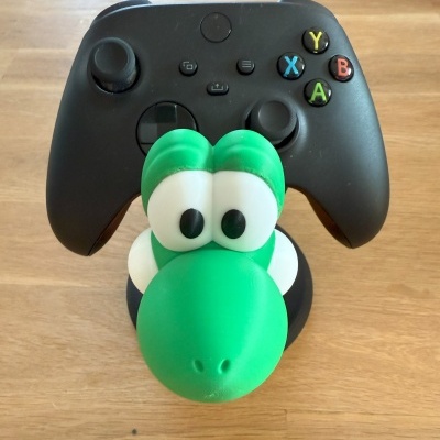 Comando de videojogos preto com botões coloridos e suporte de personagem verde em madeira clara