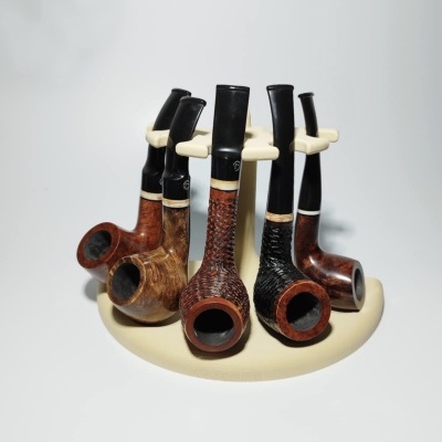 Seis cachimbos de madeira com bocais pretos em suporte creme num fundo branco.