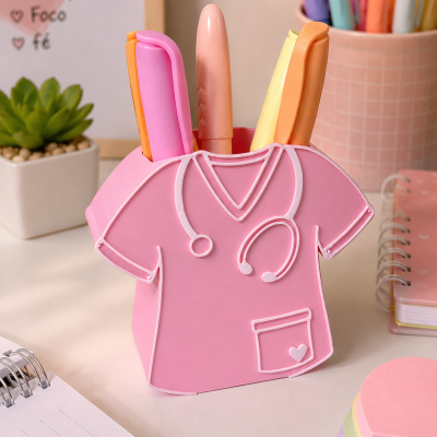 Suporte para canetas rosa em forma de bata de médico com canetas coloridas numa mesa com cadernos e planta.