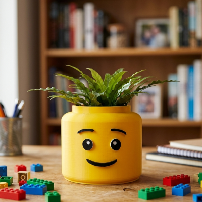 Vaso amarelo de cabeça de boneco com planta verde e peças de construção coloridas numa mesa de madeira
