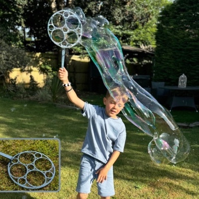 Menino a fazer bolhas de sabão gigantes com um aro azul num jardim
