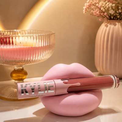 Batom líquido rosa KYLIE apoiado em escultura de lábios rosa com castiçal e vaso ao fundo