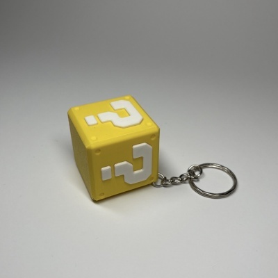 Chaveiro amarelo em forma de cubo com interrogação branca e anel metálico
