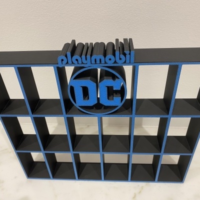 Expositor metálico preto com bordas azuis e logótipos Playmobil e DC na parte superior