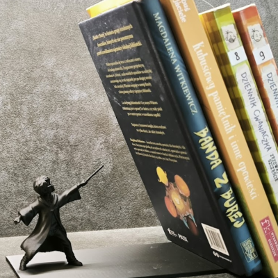 Apoio para livros com figura metálica a apontar varinha para livros coloridos apoiados