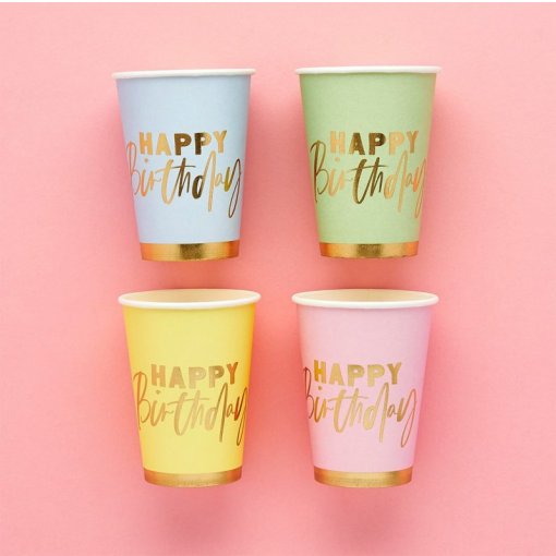 Copos de papel coloridos com texto dourado HAPPY Birthday em fundo rosa.