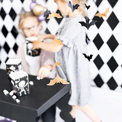 Crianças com mesa preta, caixas de pipoca com caveiras e morcegos suspensos numa sala decorada com losangos pretos e brancos