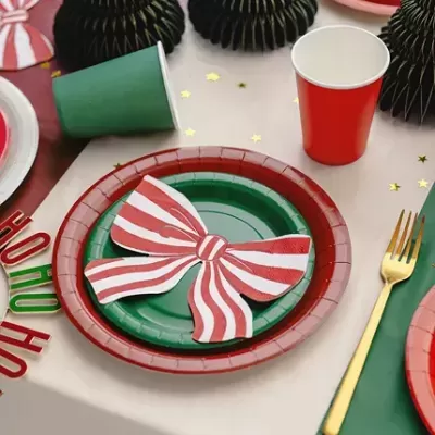 Mesa de Natal com pratos verdes e vermelhos, copos vermelho e verde, laço às riscas brancas e vermelhas, talheres dourados e árvores de papel pretas
