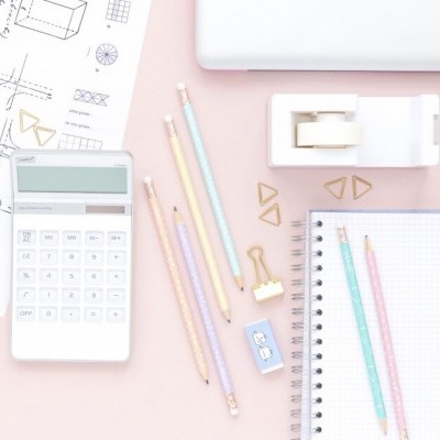 Material escolar colorido com calculadora, lápis, borracha, clips triangulares, fita adesiva e caderno em fundo rosa