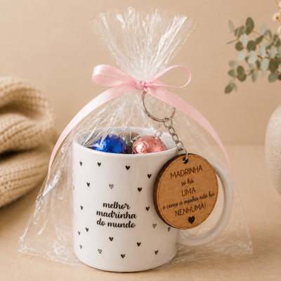 Caneca branca com corações pretos e texto para madrinha, embrulhada com chaveiro e bombons.
