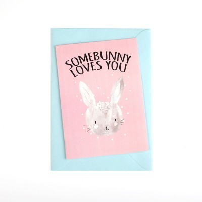 Cartão rosa com ilustração de coelho e texto 'SOMEBUNNY LOVES YOU', com envelope azul claro.