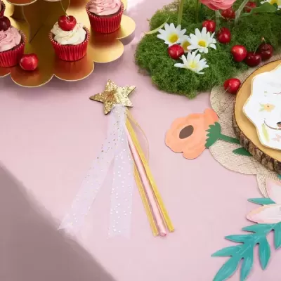 Varinha mágica e cupcakes sobre mesa decorada com flores artificiais