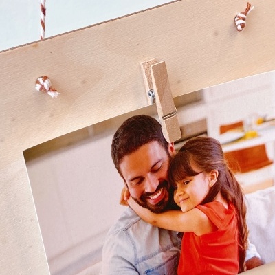 Fotografia impressa de um homem e uma menina abraçados, presa por molhador a moldura de madeira clara.
