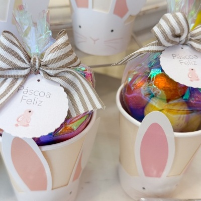 Caixas em forma de coelho com sacos de ovos de chocolate coloridos e etiquetas a dizer 'Páscoa Feliz'