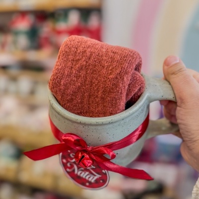 Caneca cinzenta com fita vermelha e meias dentro, etiqueta com 'Natal'