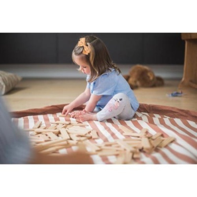 Menina a brincar com blocos de madeira num tapete riscado