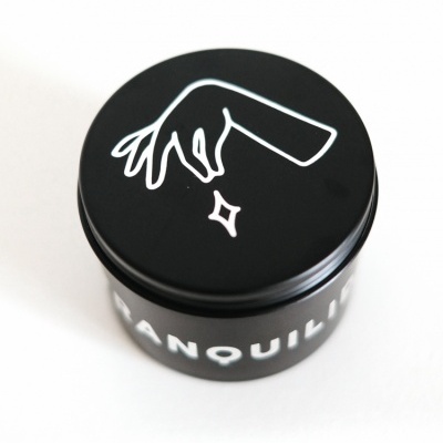 Frasco preto com tampa e desenho branco de mão estilizada e palavra 'TRANQUILI'