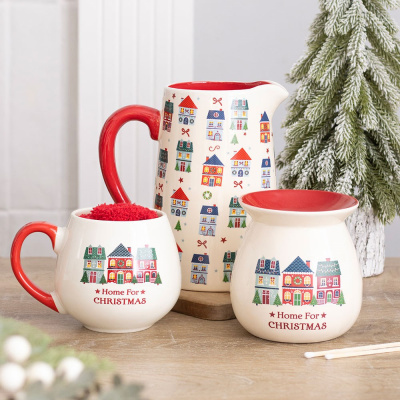 Conjunto de cerâmica com tema de Natal, incluindo jarro, caneca e vela decorativa com casas coloridas e texto natalício.