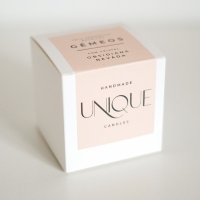 Caixa branca cúbica com etiqueta cor de rosa e texto sobre vela artesanal