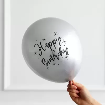 Balão prateado com texto 'Happy Birthday' segurado por uma mão