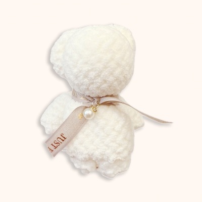 Ursinho de peluche branco com fita bege e acessórios, visto de costas