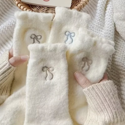 Meias de lã creme bordadas com laços em cores várias seguradas por mãos com camisolas creme ao fundo uma cesta de verga