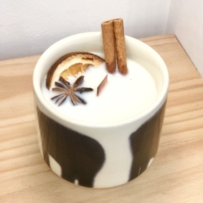 Vela perfumada com decoração natural num recipiente de cerâmica branca e preta.