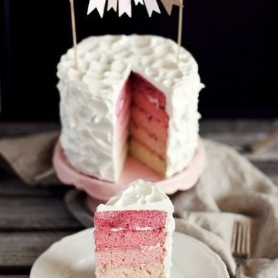 Bolo com camadas em degradê e cobertura branca com decoração de bandeirola